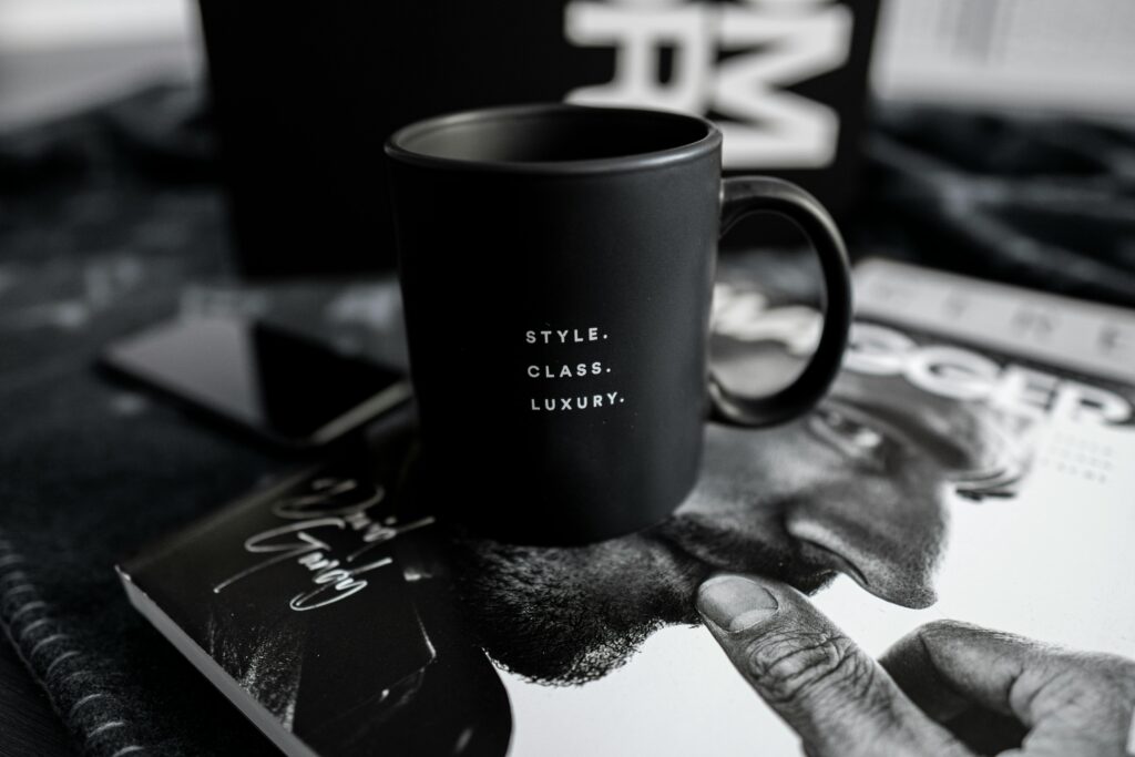 A stylish black mug with text sits on a luxury magazine, presenting an elegant and modern lifestyle setting indoors.